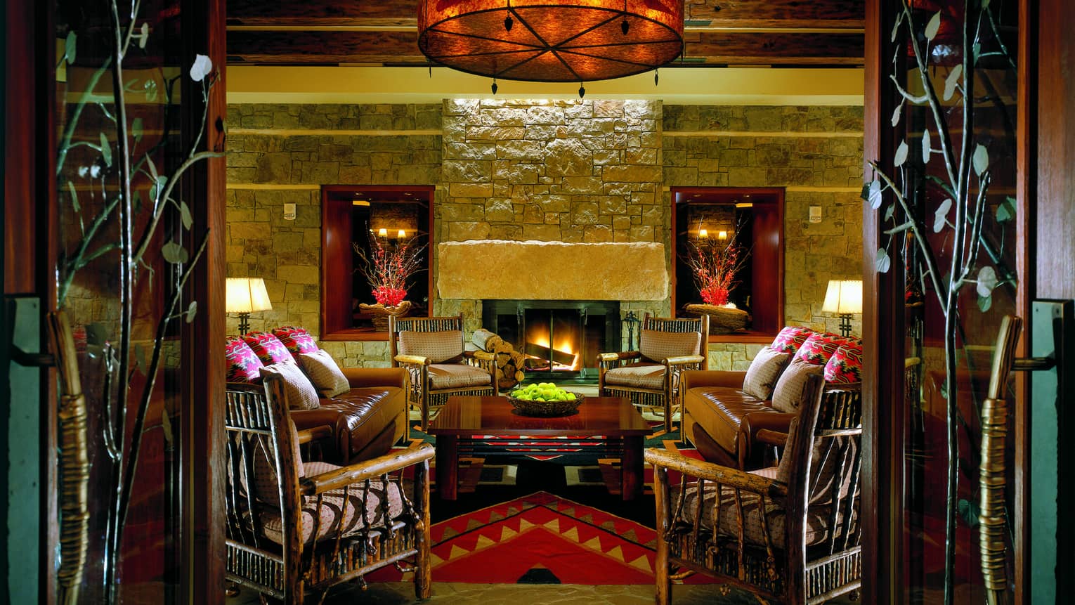 A dimly lit stone room with red accents, a circle of couches and chairs at the center