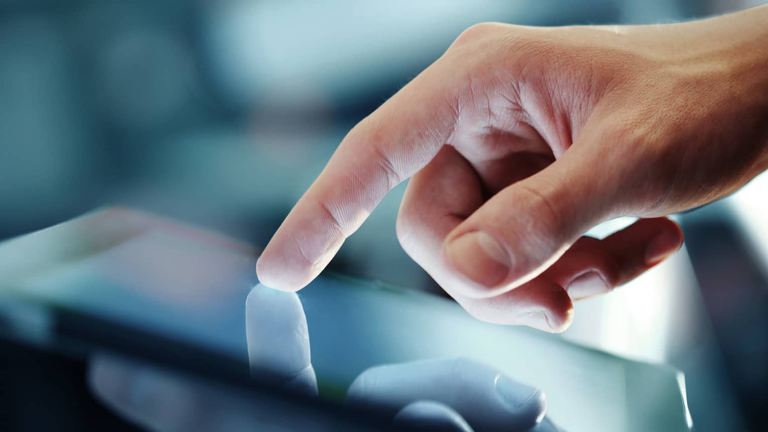 A hand with index finger extended touches the screen of a tablet