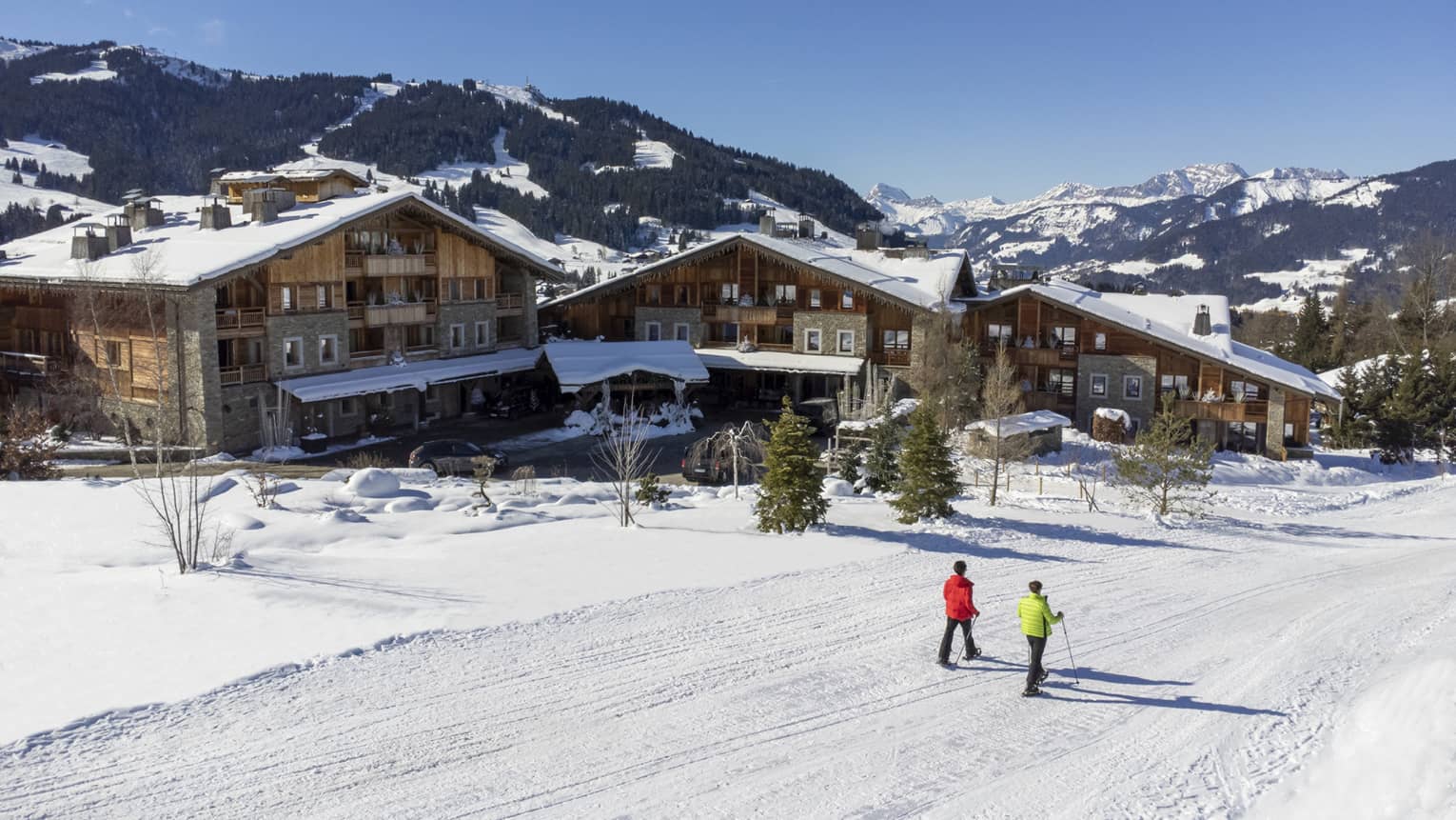 Two people show shoeing on snow-covered path in front of Four Seasons Hotel Megeve with Alps in backdrop