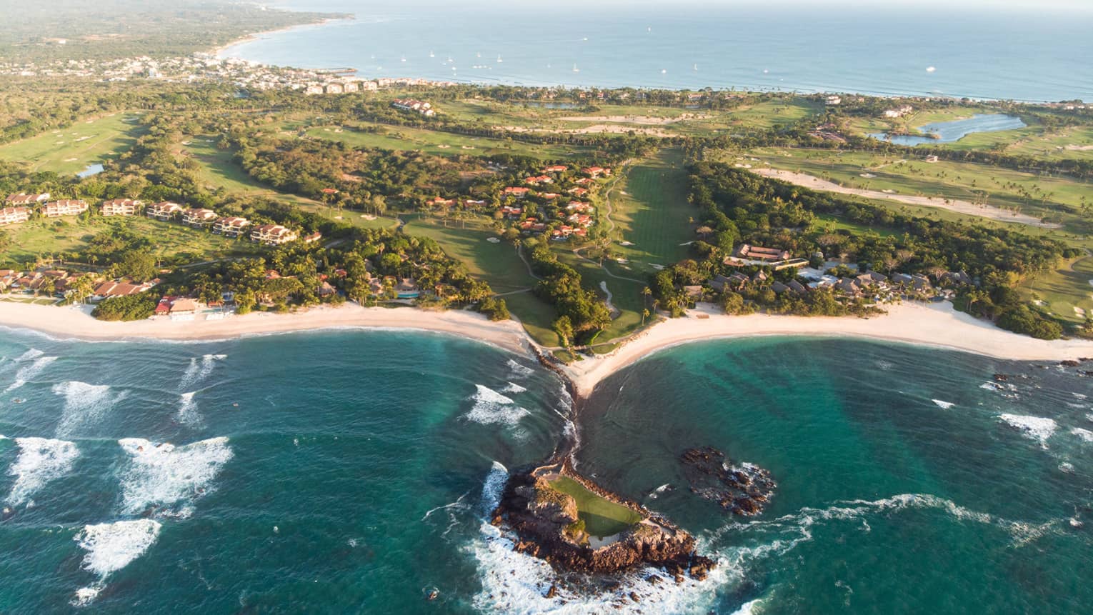 A coastline with deep blue water running up against sand and plants.