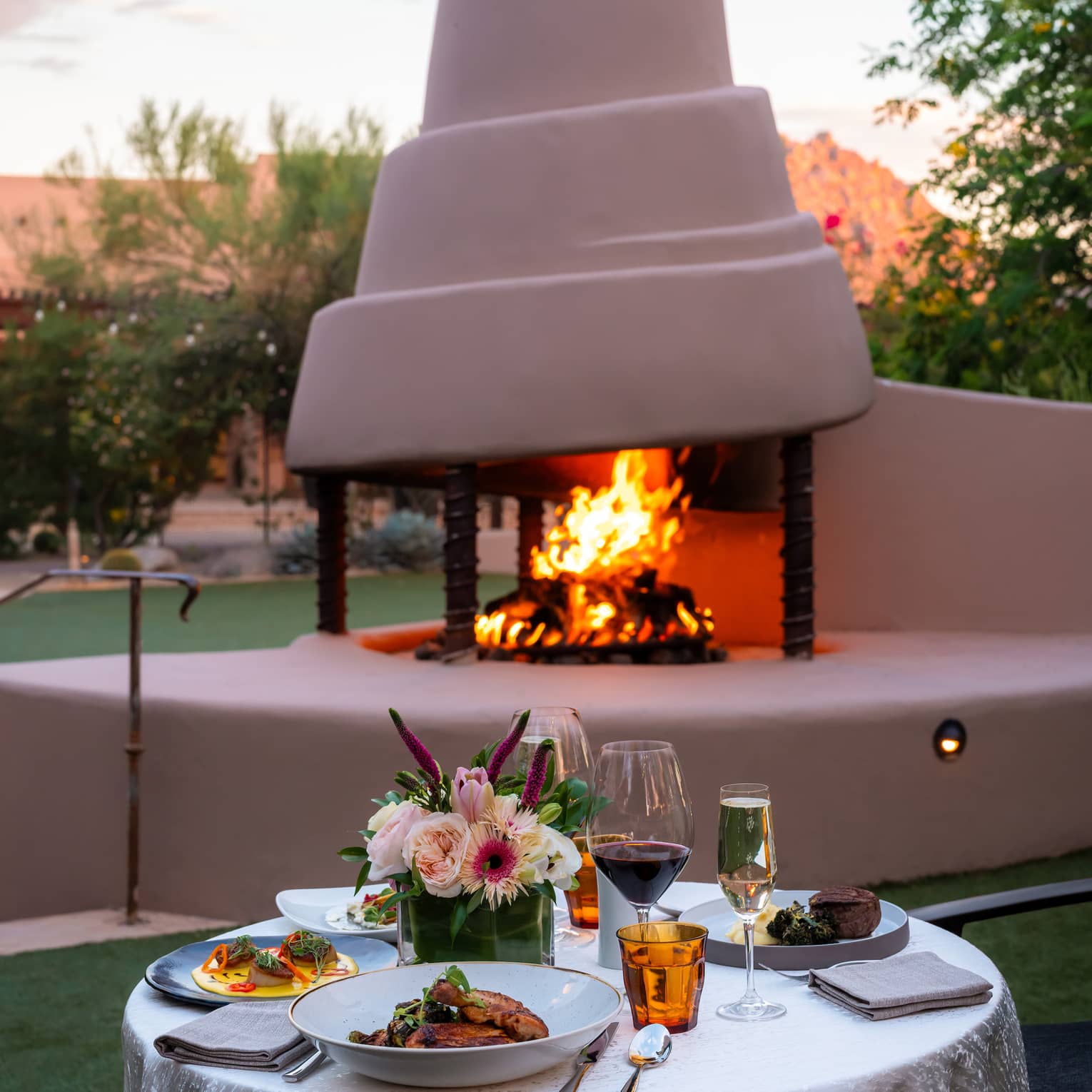 An outdoor dining table set with dishes and glasses near a fire pit