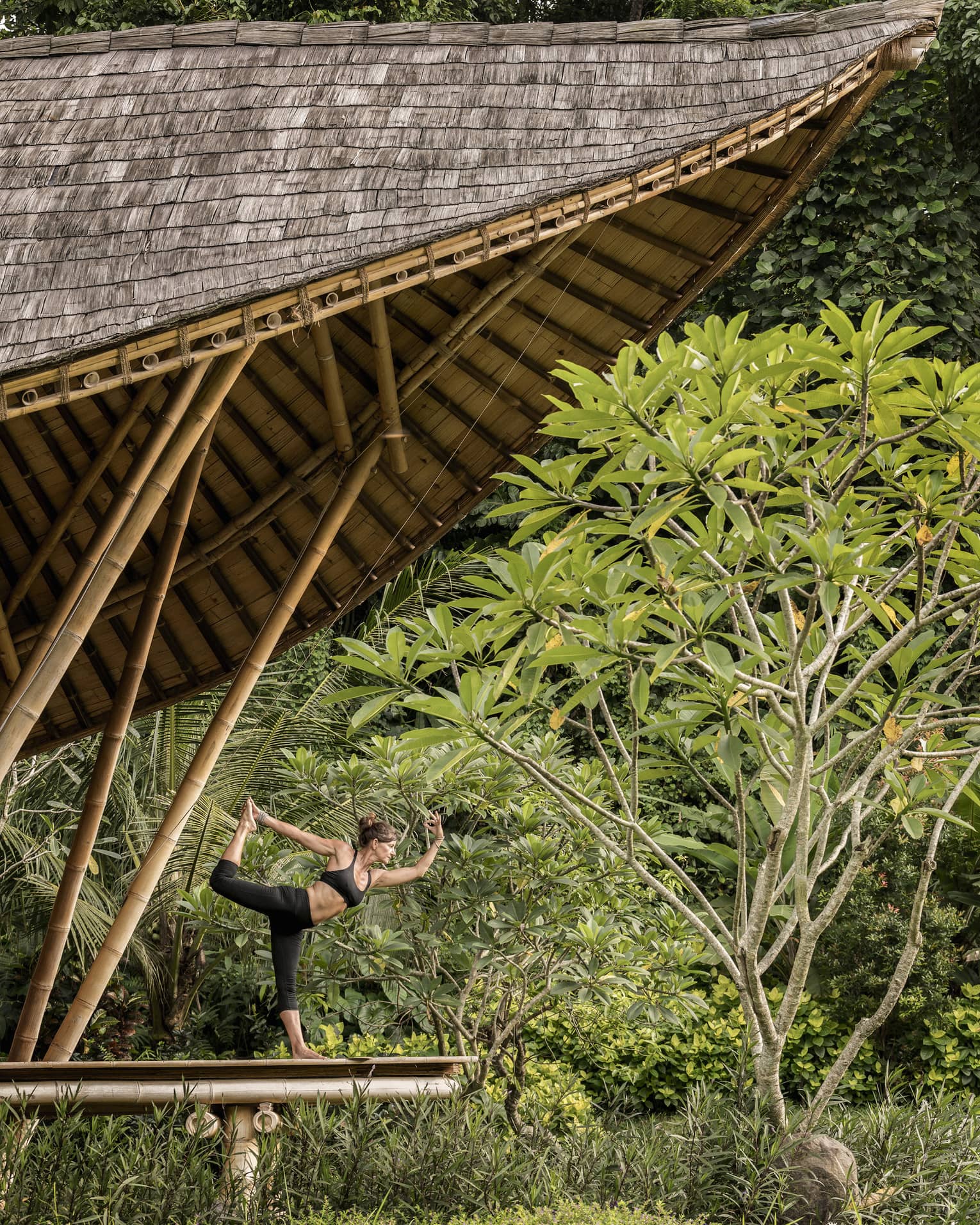A guest with her arms and leg outstretched, doing yoga in an outdoor pavilion 