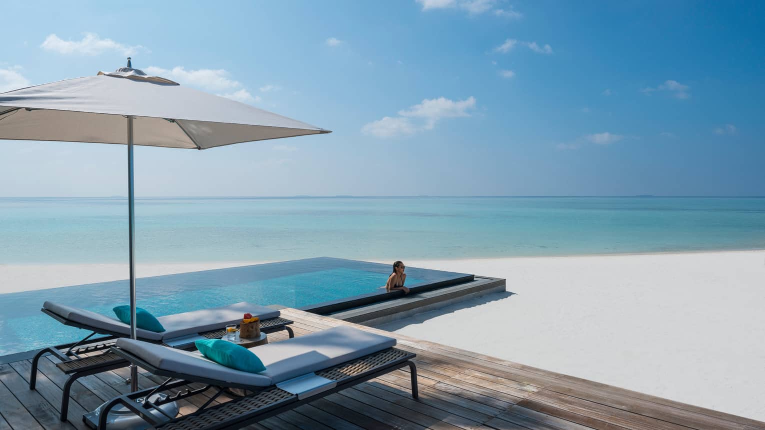Woman leans against ledge of private infinity pool off Beach Villa patio, beach