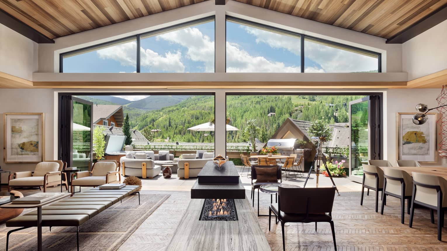 Luxurious mountain villa interior with an open-plan living area, modern fireplace, and expansive glass doors leading to an outdoor terrace with panoramic forest views.