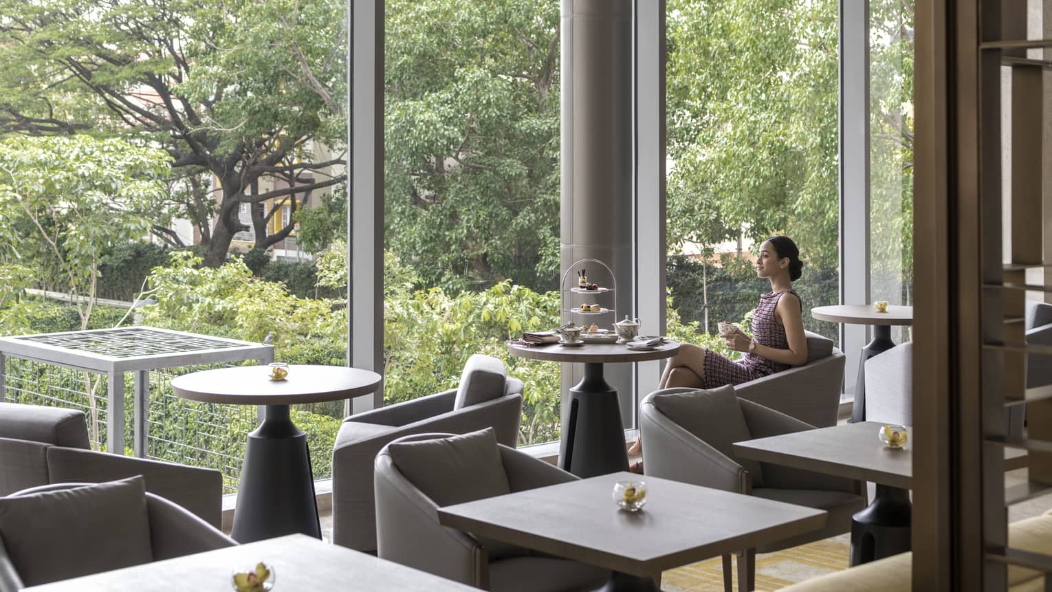 A woman sips a up of coffee as she enjoys the view out a large window