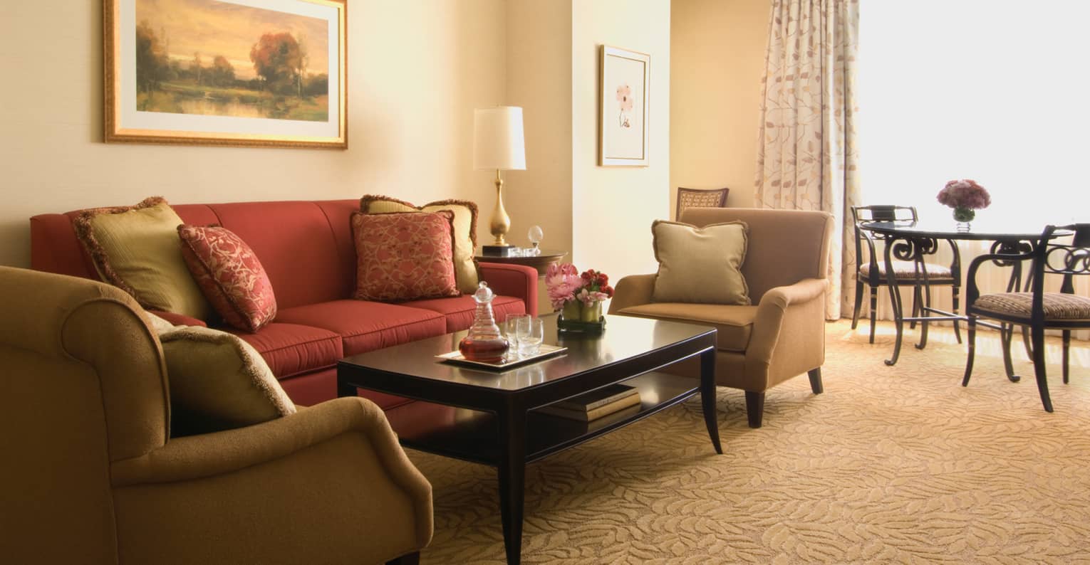 One-Bedroom Suite red sofa, two beige armchairs around black coffee table, dining room, sunny window