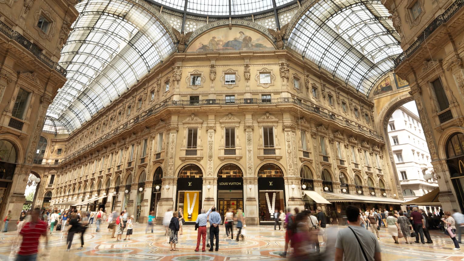 Shoppers gathered in  historic Galleria Vittorio Emanuele building with soaring ceilings, shops