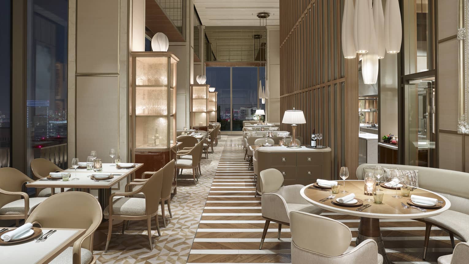 Restaurant with off-white chairs and sofas, elegant chandeliers, windows with nighttime views