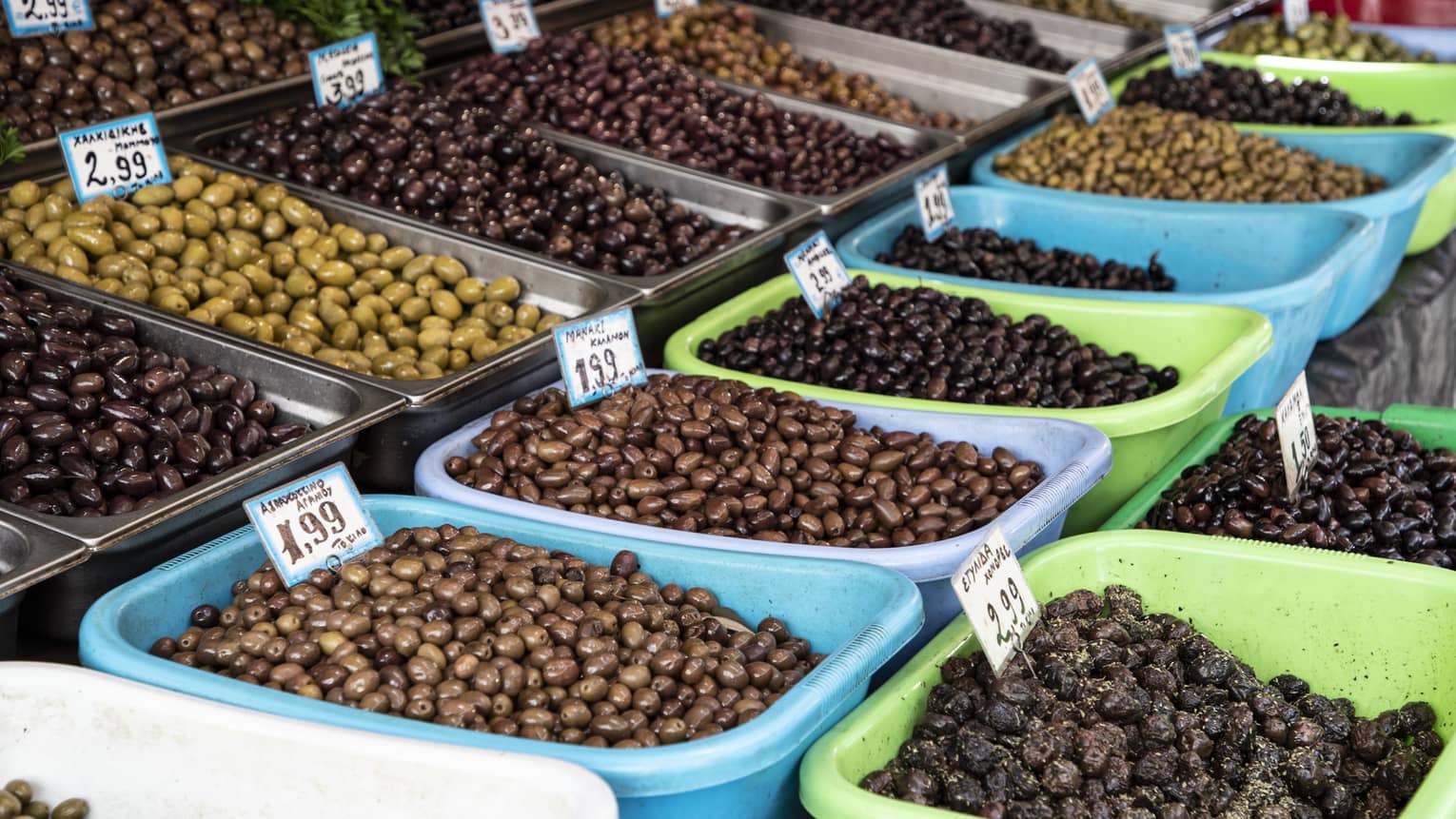 A wide assortment of olives displayed in rows of metal and plastic bins, each marked with the type of olive and the price.