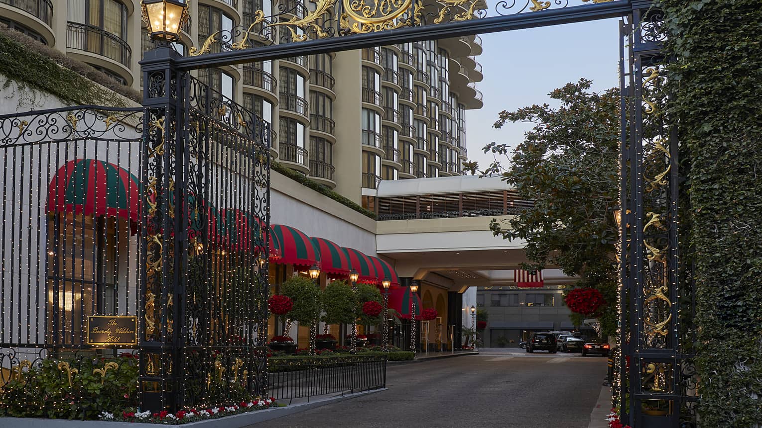 A metal gate with gold decoration at the entrance to a long driveway next to a hotel.