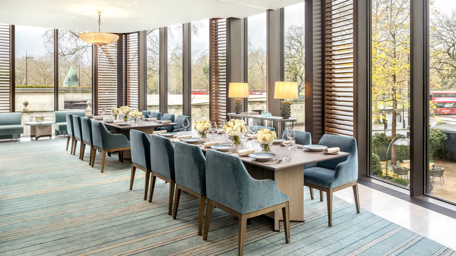 Two rectangular dining tables flanked with blue suede?covered chairs, set for a meal