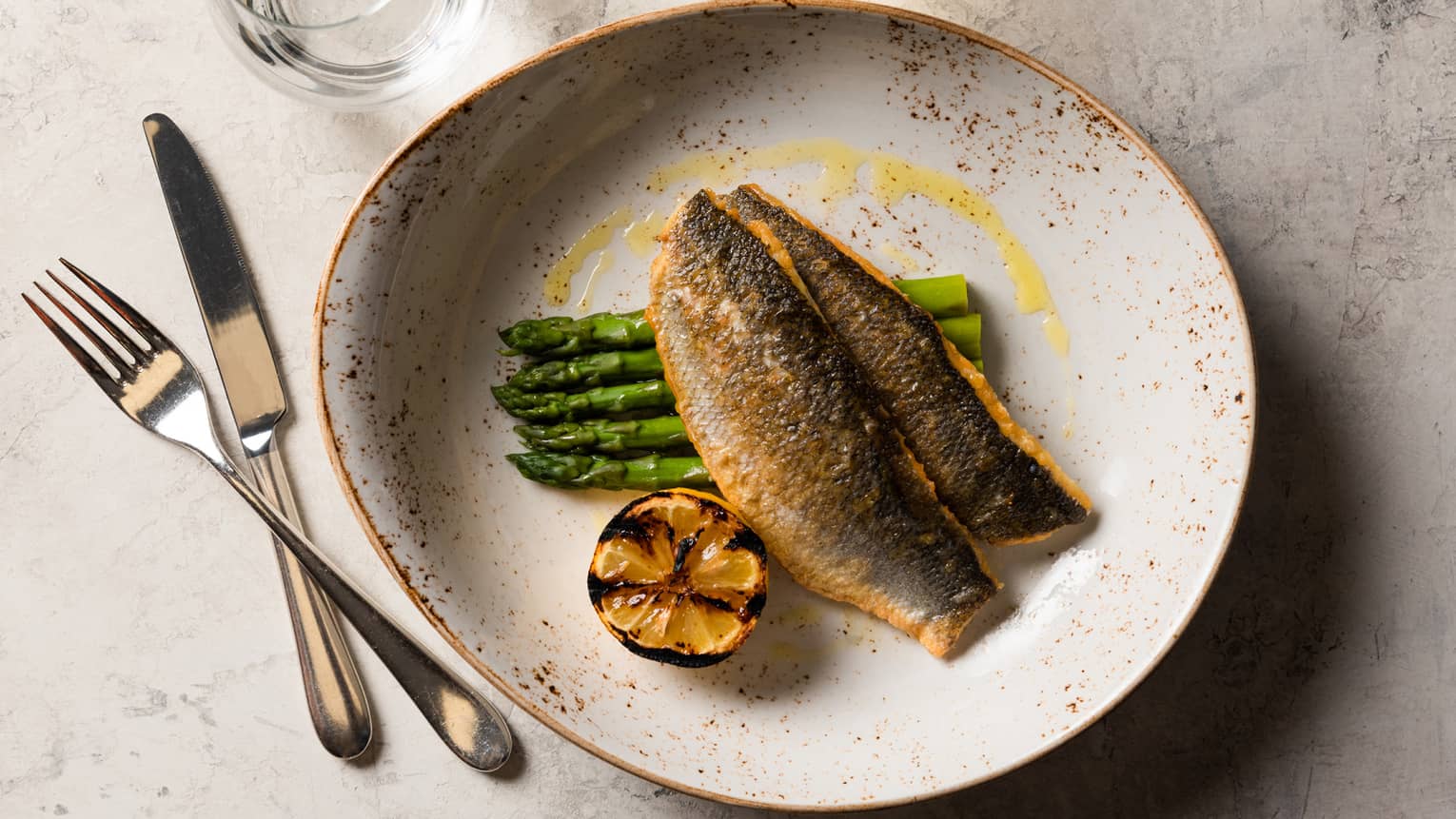 Cooked fish with asparagus and garlic on a grey plate.