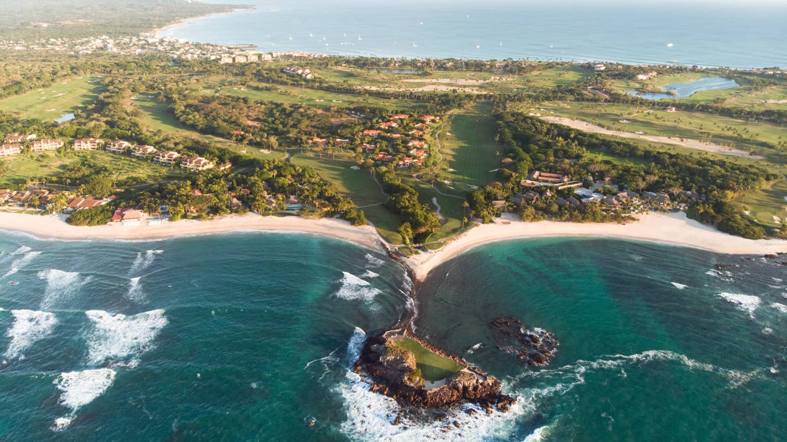 A coastline with deep blue water running up against sand and plants.