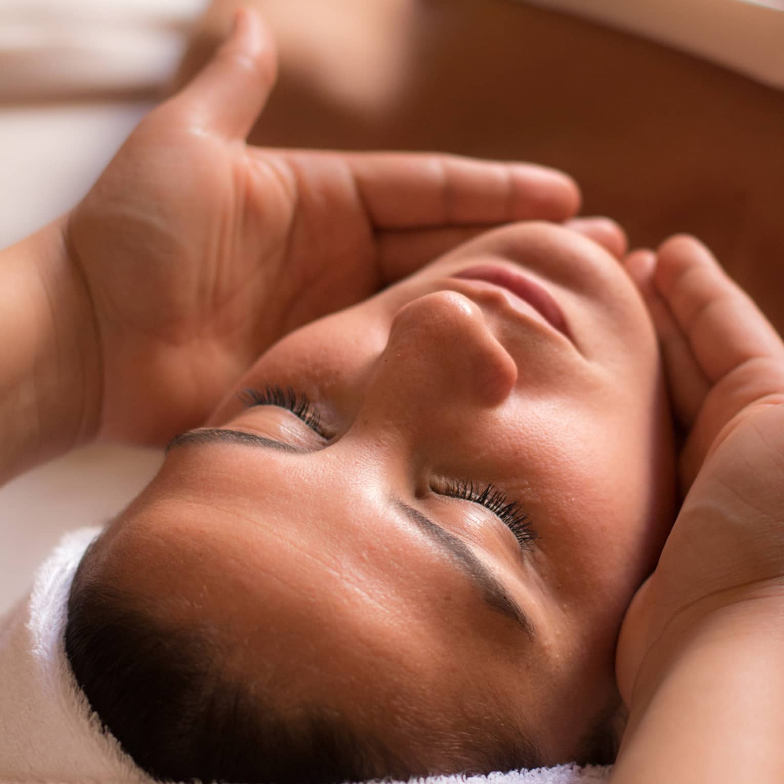 Close-up of woman with eyes closed facing up as hands cup her face and chin