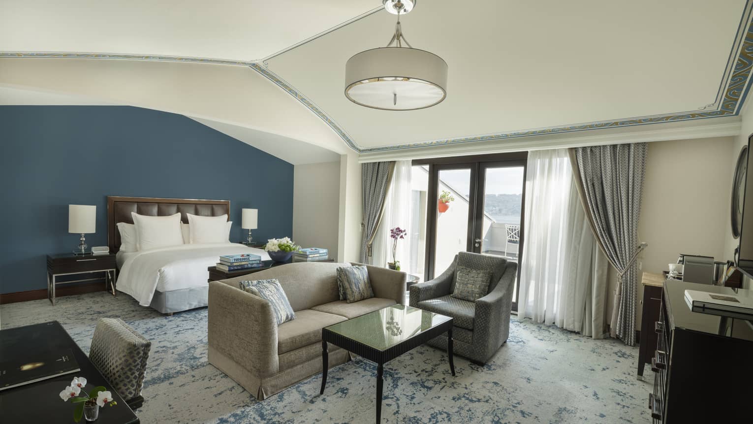 Elegant hotel suite featuring a king bed and sitting area with a sofa, arm chair and coffee table, plus a walk-out rooftop terrace