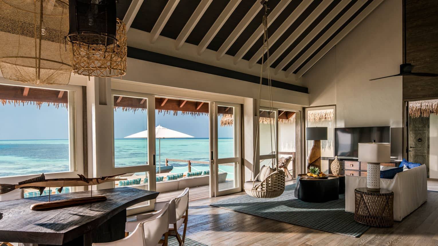 Two-Bedroom Water Villa rustic dining table, seating area with hanging wicker chair under soaring ceilings