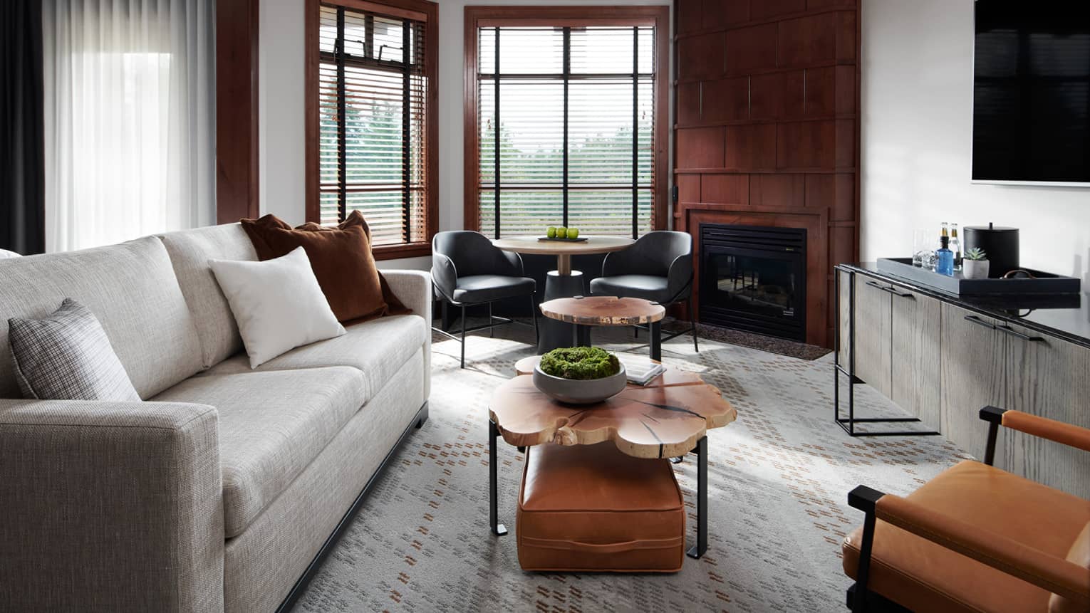 Sophisticated interior of a deluxe room at Four Seasons Whistler. The living space features elegant wood paneling, large windows with blinds, and a mix of modern furnishings including a plush gray sofa, leather armchairs, round wooden coffee tables, and a sleek black media console with a mounted flat-screen TV. A contemporary fireplace adds a cozy ambiance to the room.,Sophisticated interior of a deluxe room at Four Seasons Whistler. The living space features elegant wood paneling, large windows with blinds, and a mix of modern furnishings including a plush gray sofa, leather armchairs, round wooden coffee tables, and a sleek black media console with a mounted flat-screen TV. A contemporary fireplace adds a cozy ambiance to the room.