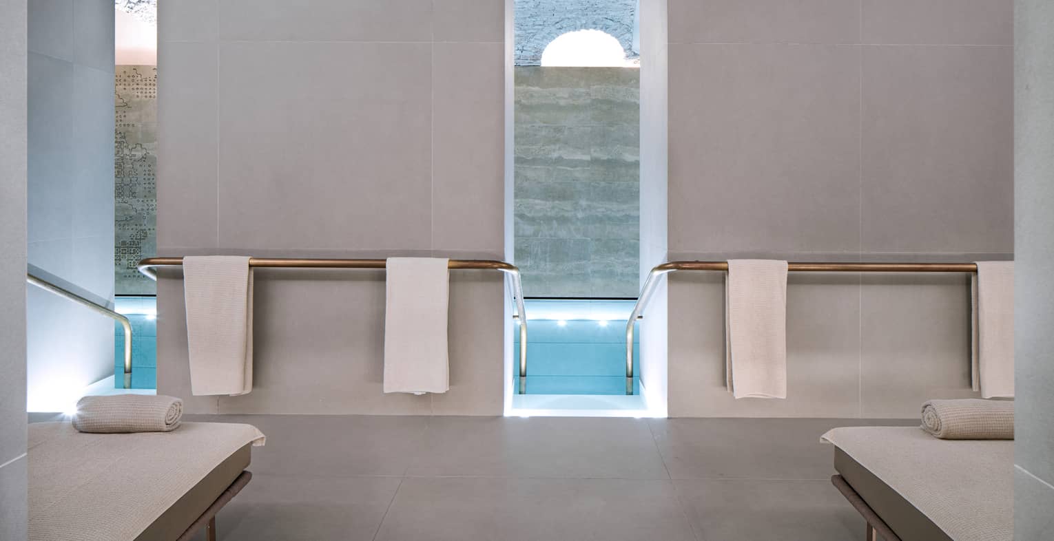 Concrete spa pool deck with white spa loungers, white towels hanging and pool entry between tall white walls