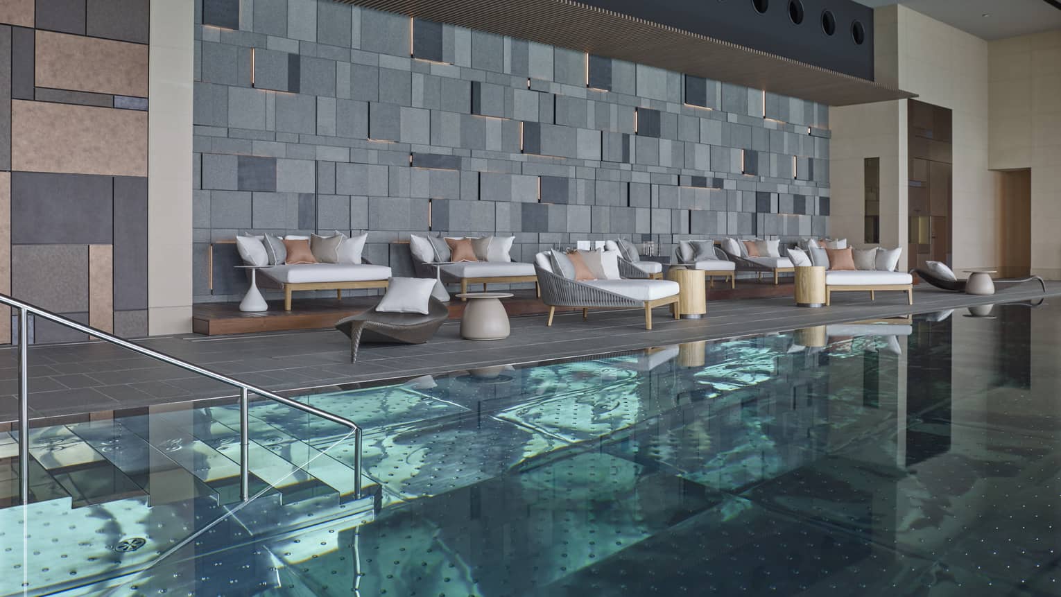 Indoor swimming pool, plush patio chairs on deck under modern brick wall
