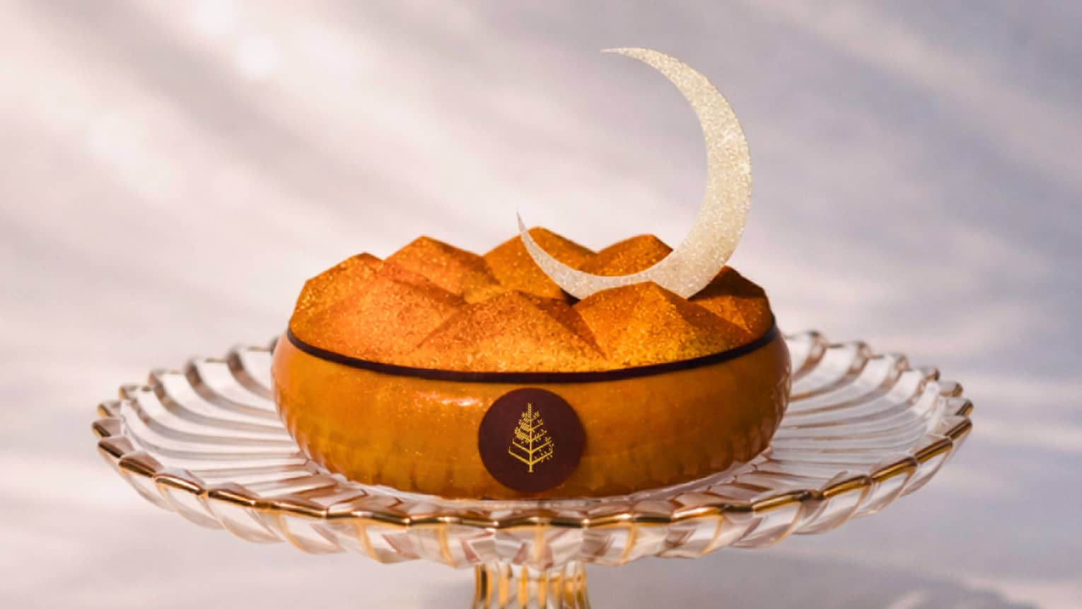 Cake topped with a decorative crescent moon served on a glass cake stand