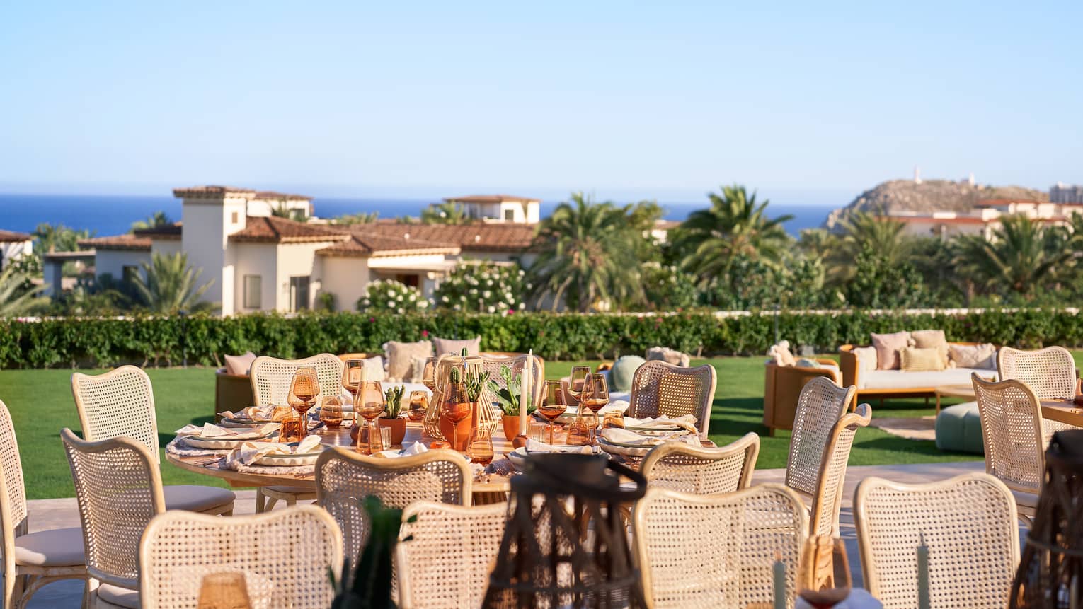 Tables placed and set for an event on a vast lawn, with trees, buildings and the coastal horizon in the background