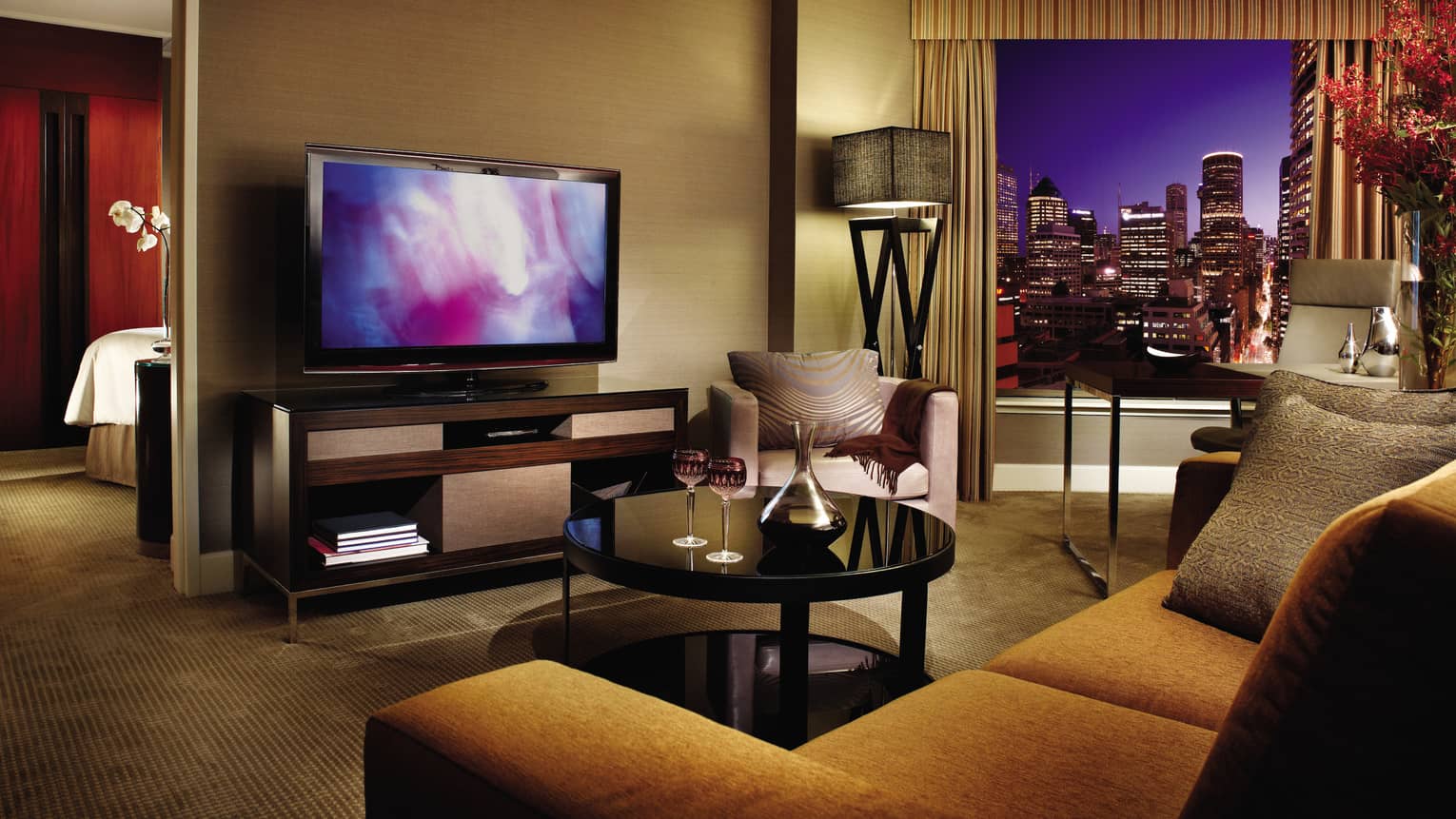 Club City Suite gold upholstered sofa, table with wine glasses, TV, bedroom door at night