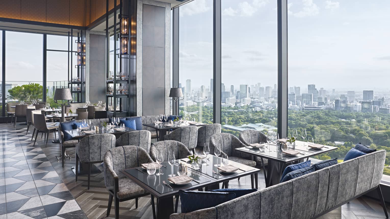 Restaurant with square tables and grey chairs/sofas, black-and-white tile floor, wall of windows looking out to Imperial Gardens in Tokyo