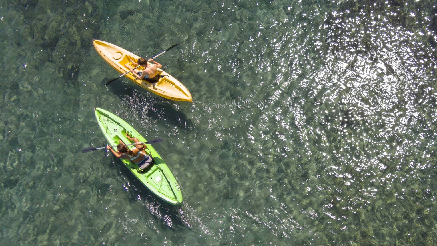 Aerial view of man and woman in green and orange kayaks on reef
