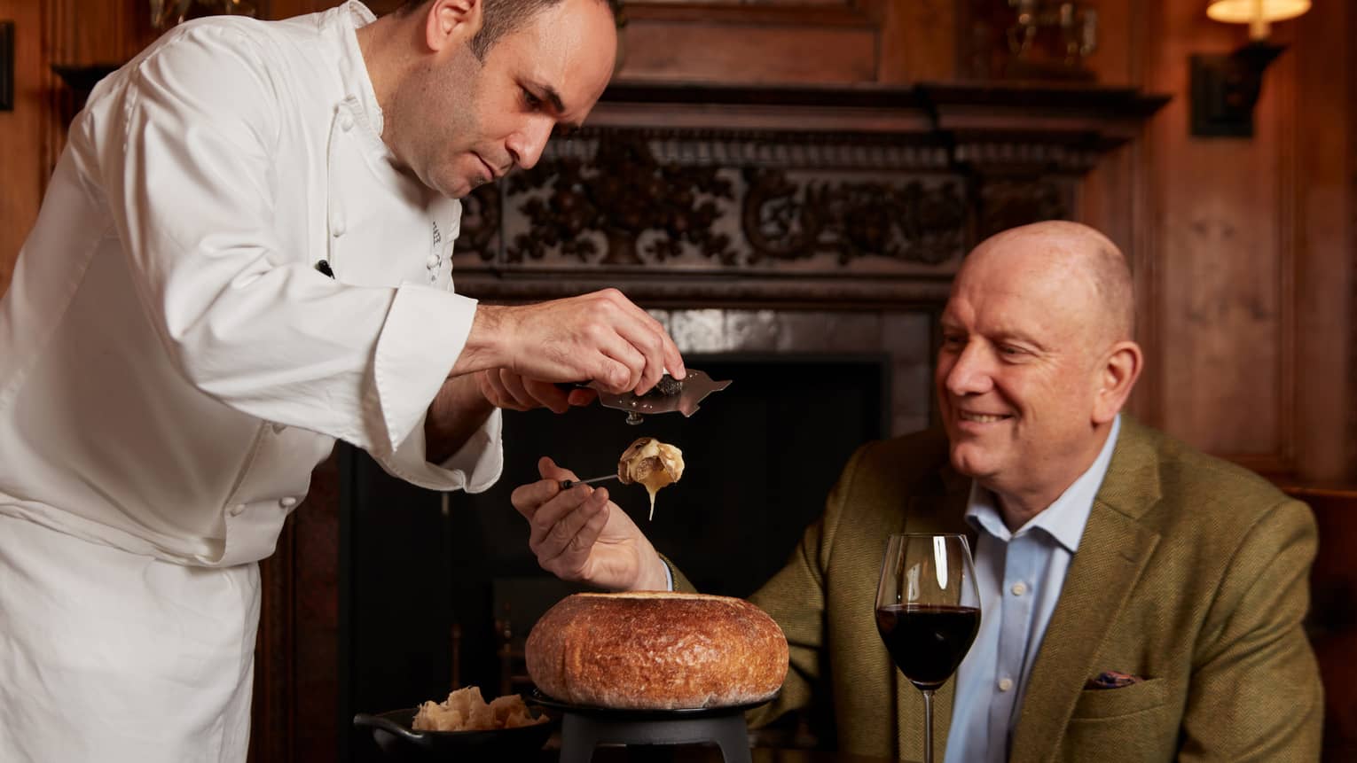 General Manager Andrew Harrison holds up a fondue fork with bread and raclette while chef grates nutmeg on it