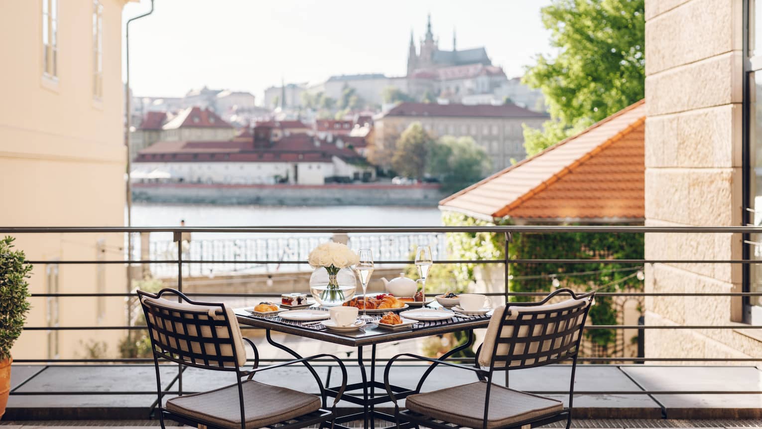 Terrace with iron bistro table set for a meal, overlooking the river and Prague Castle