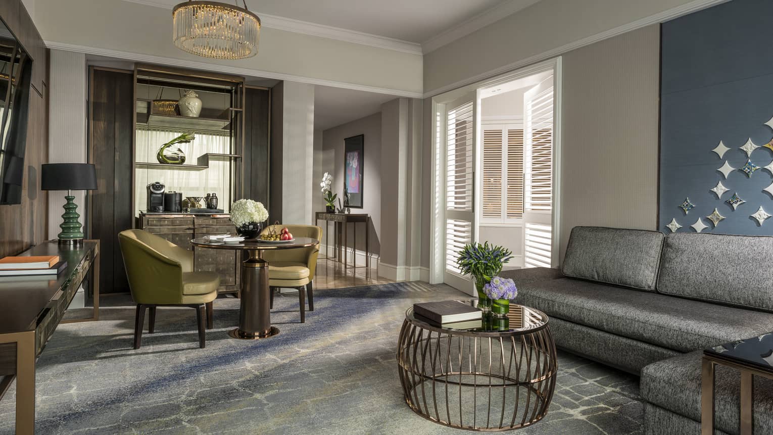 Gold dining chairs around small dining table by brass wire table, L-shaped grey sofa