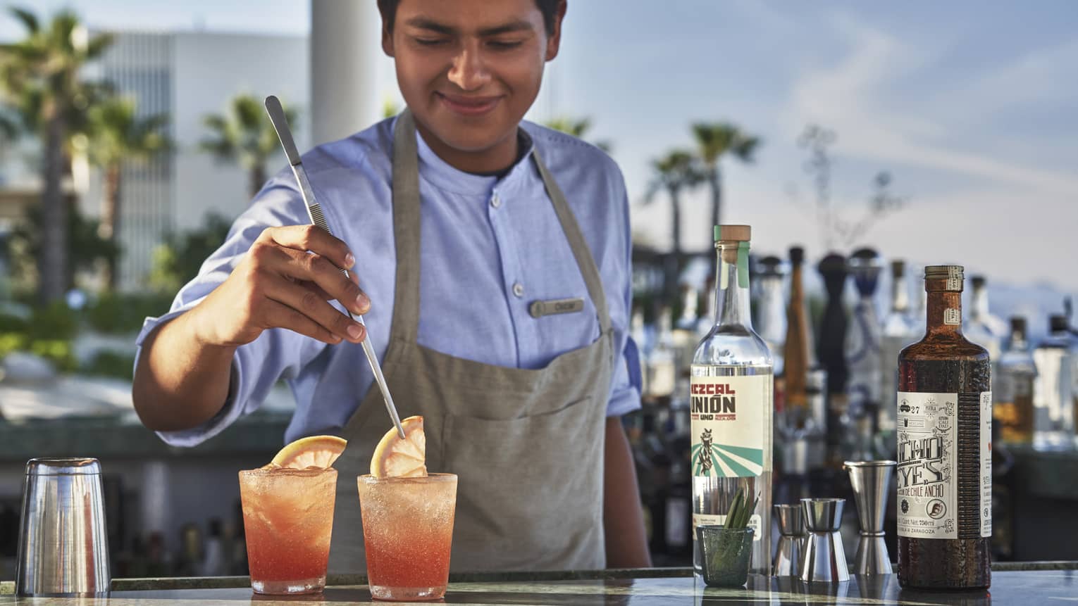 A Casa de Brasa mixologist garnishes two pink cocktails with a slice of citrus at an our door bar 