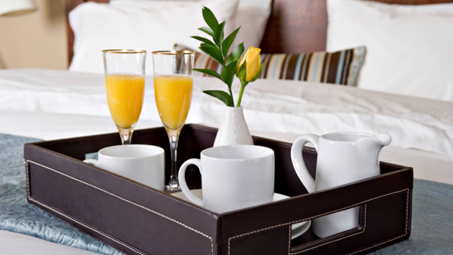 Close-up of in-room dining tray with two champagne and orange juice glasses, white coffee mugs, yellow flower