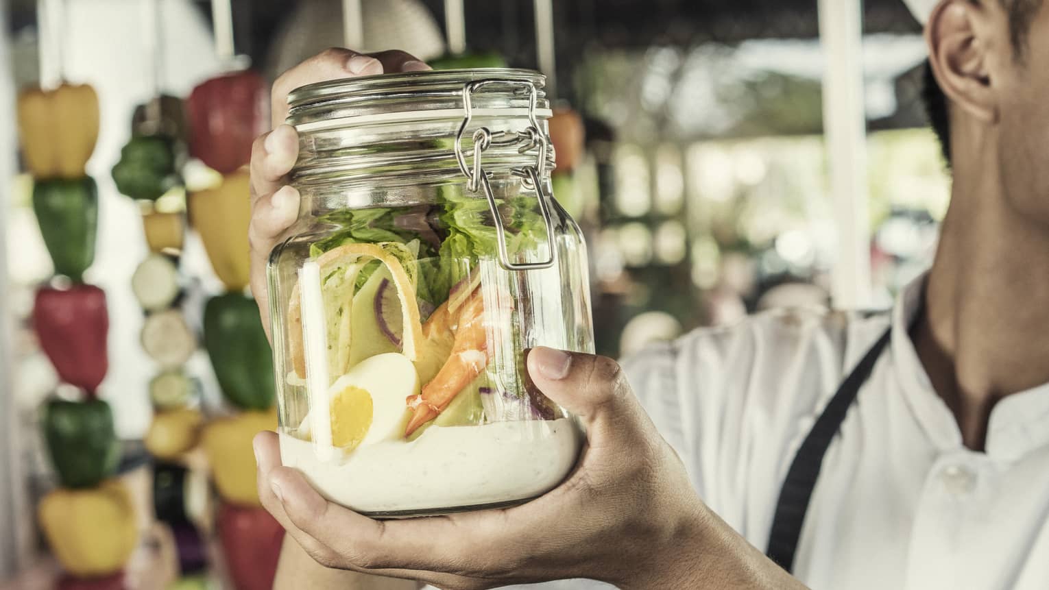 A chef shakes a caesar salad in a glass jar with some dressing