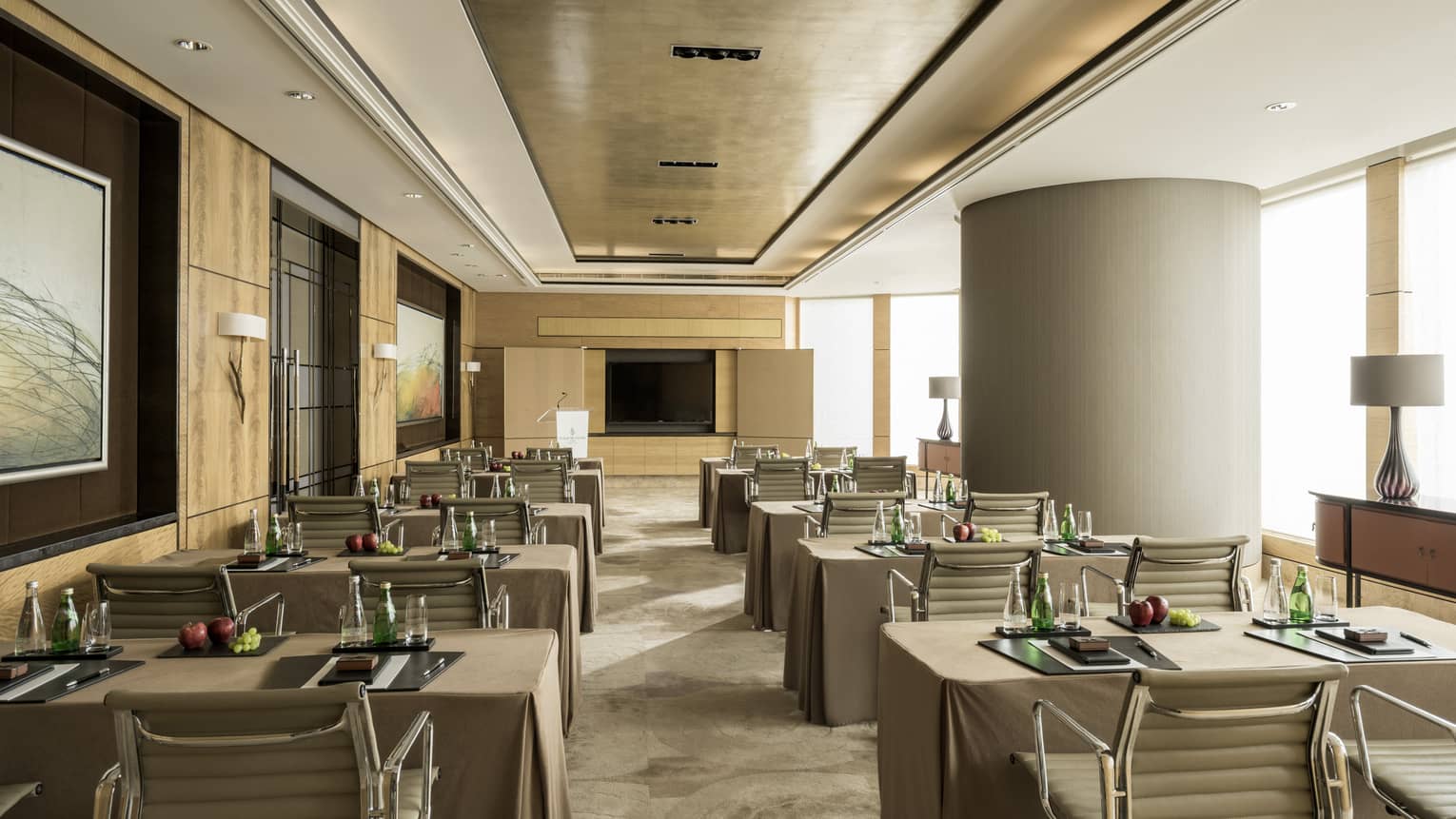 Conference room with rows of small tables, pairs of chairs facing screen, large pillar 