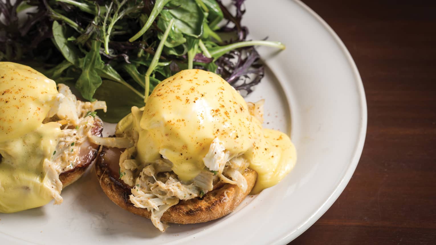 Close-up of Crab Benedict on white plate, bread with crab meat and poached egg, smothered in Hollandaise sauce