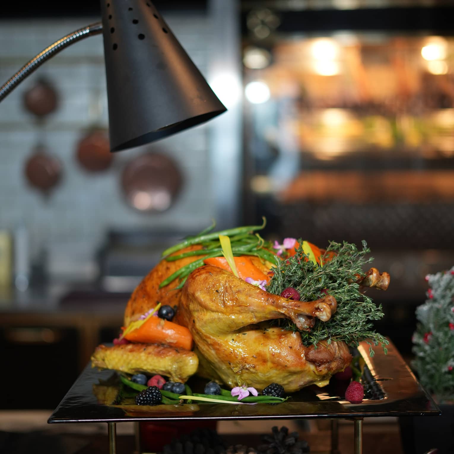 Whole roasted turkey garnished with vegetables sits on a silver platter beneath a black lantern
