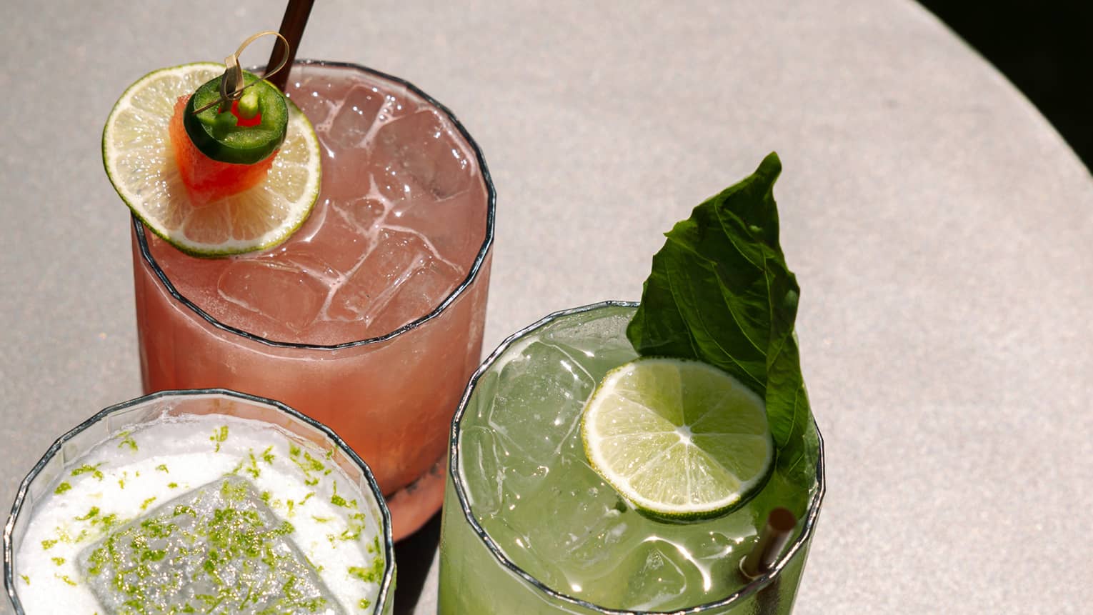 Three alcoholic beverages with lime slices in them.