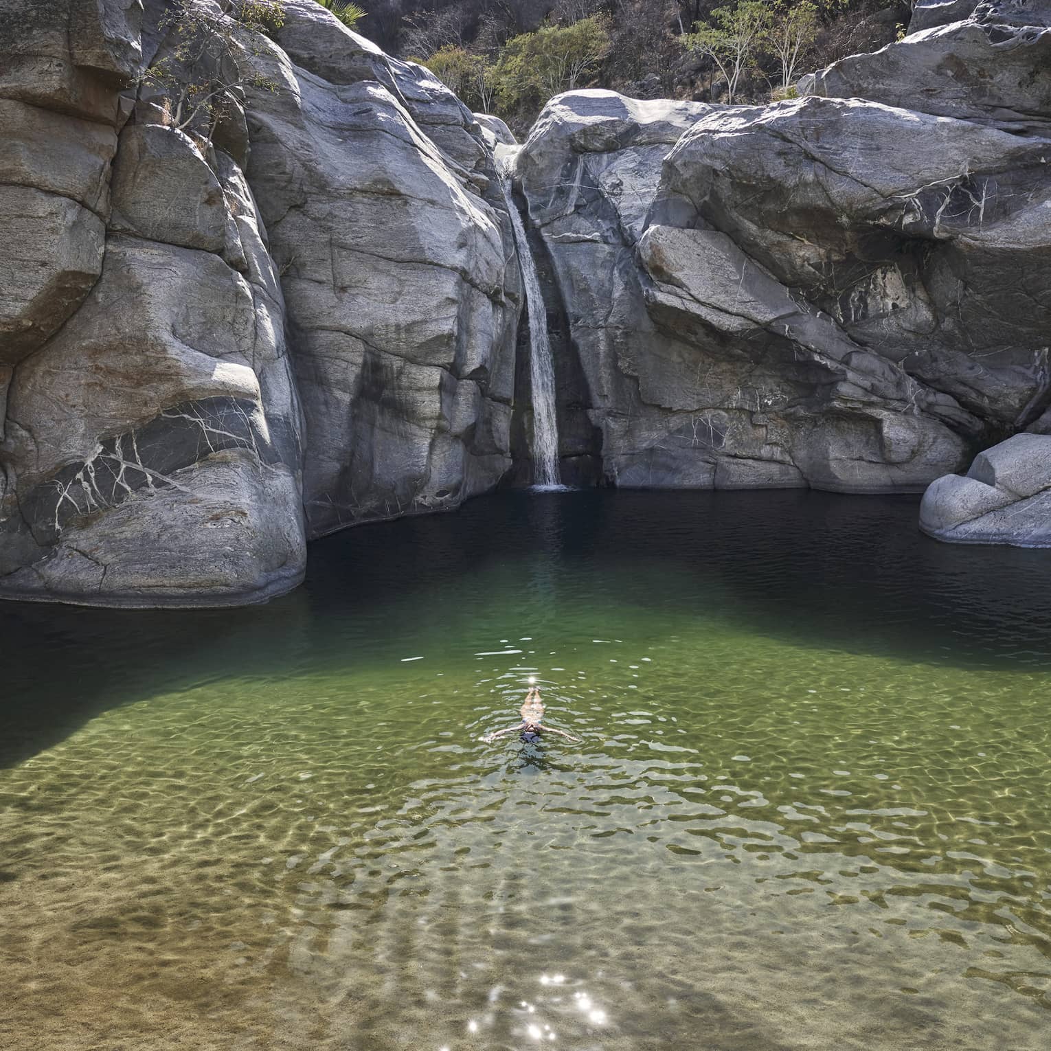 A person in a small well of water surrounded by large rock faces and trees.