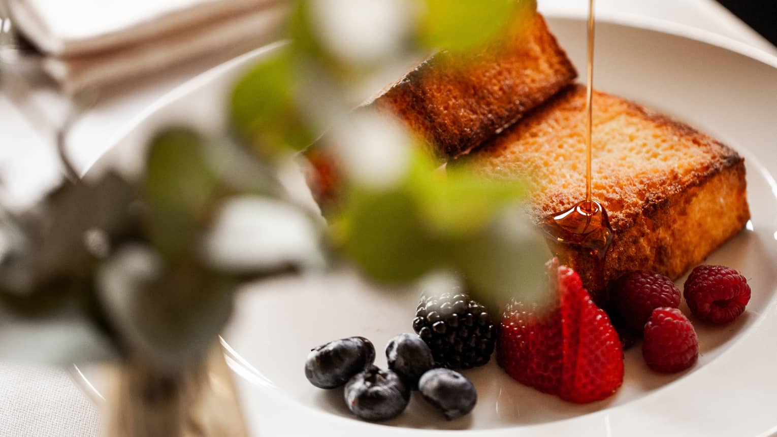 Syrup being poured over French toast with mixed berries
