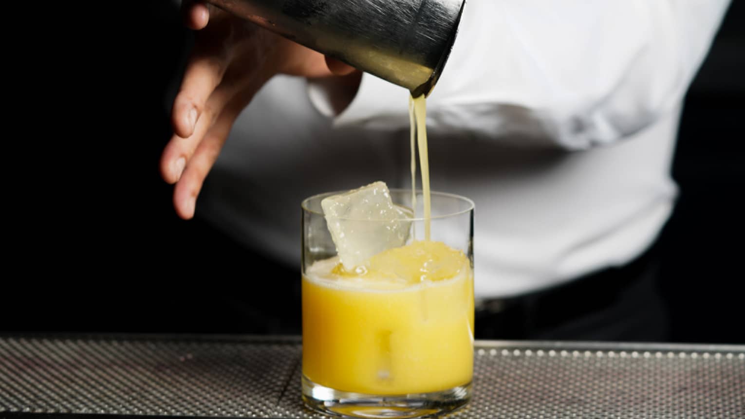 ,A bartender pours a yellow drink into a glass from a cocktail shaker