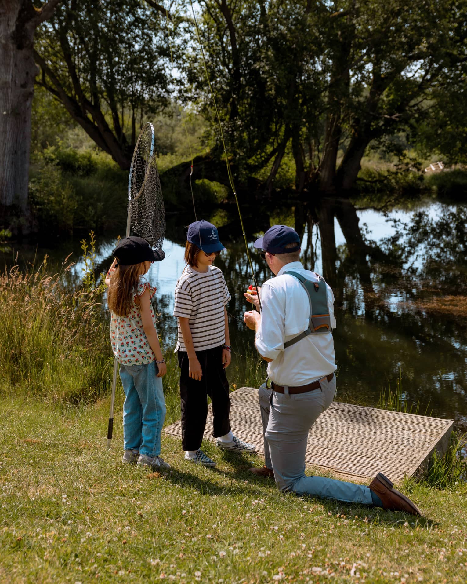 Fishing instructor holding fishing rod and kneeling in front of two children with one holding a net