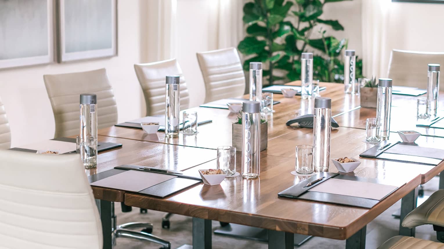 A rectangular boardroom table set with clear glass water bottles and black folders in a naturally-lit room