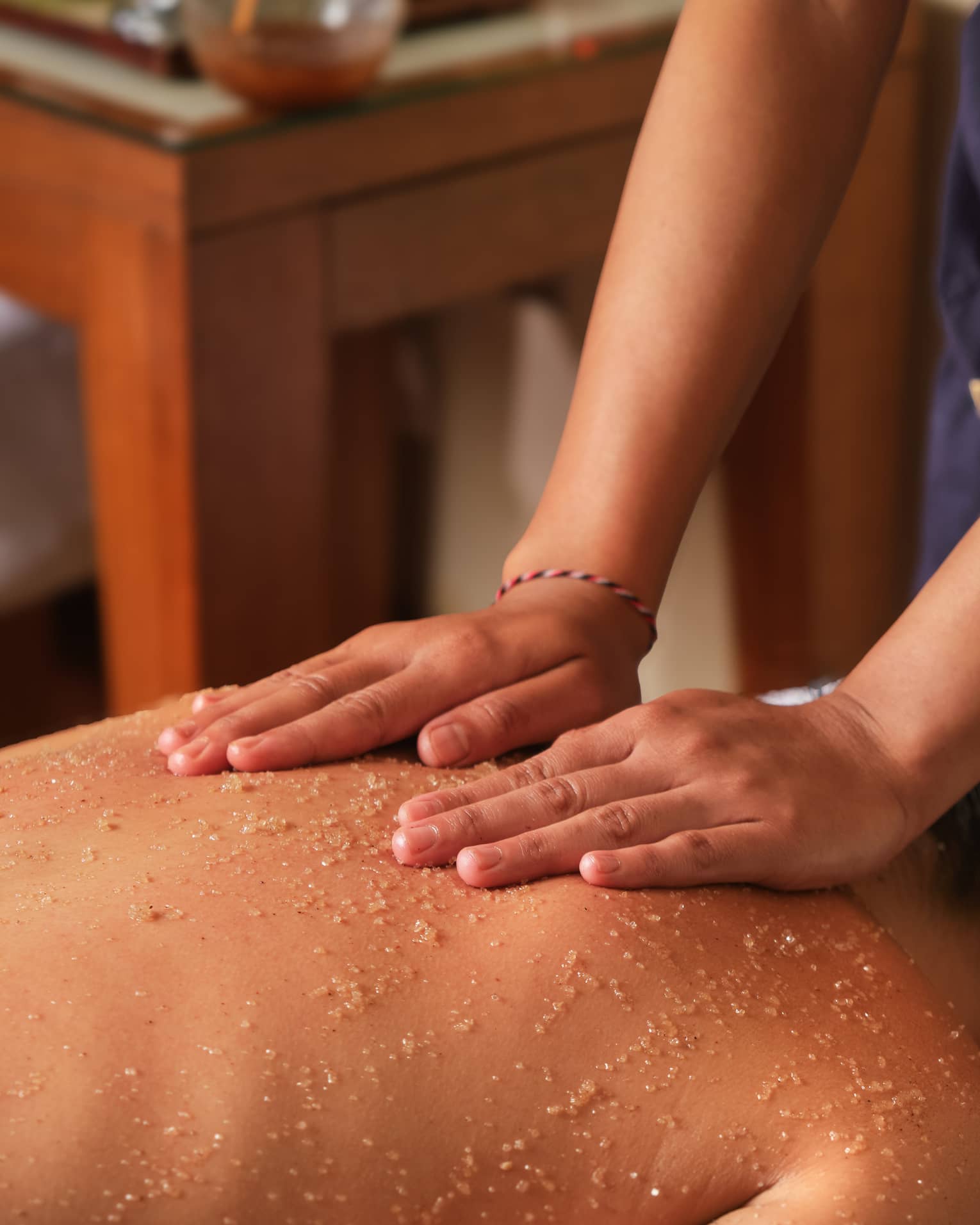 A spa attendant applies a scrub to a guest's back