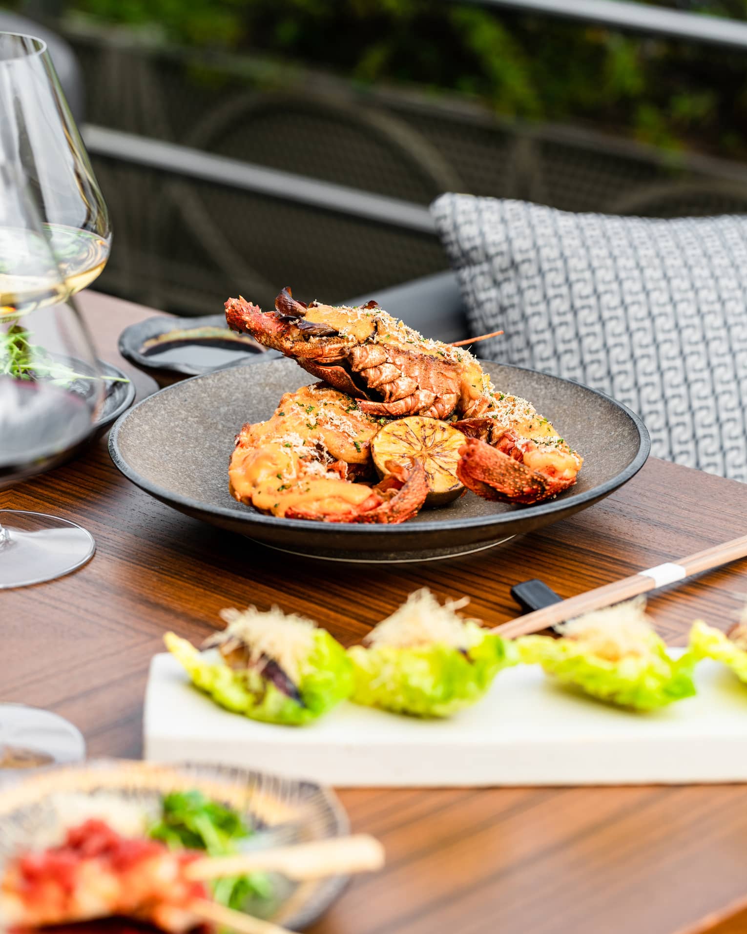 Spiny Lobster Thermidor on brown ceramic dish set on a wooden table with chopsticks