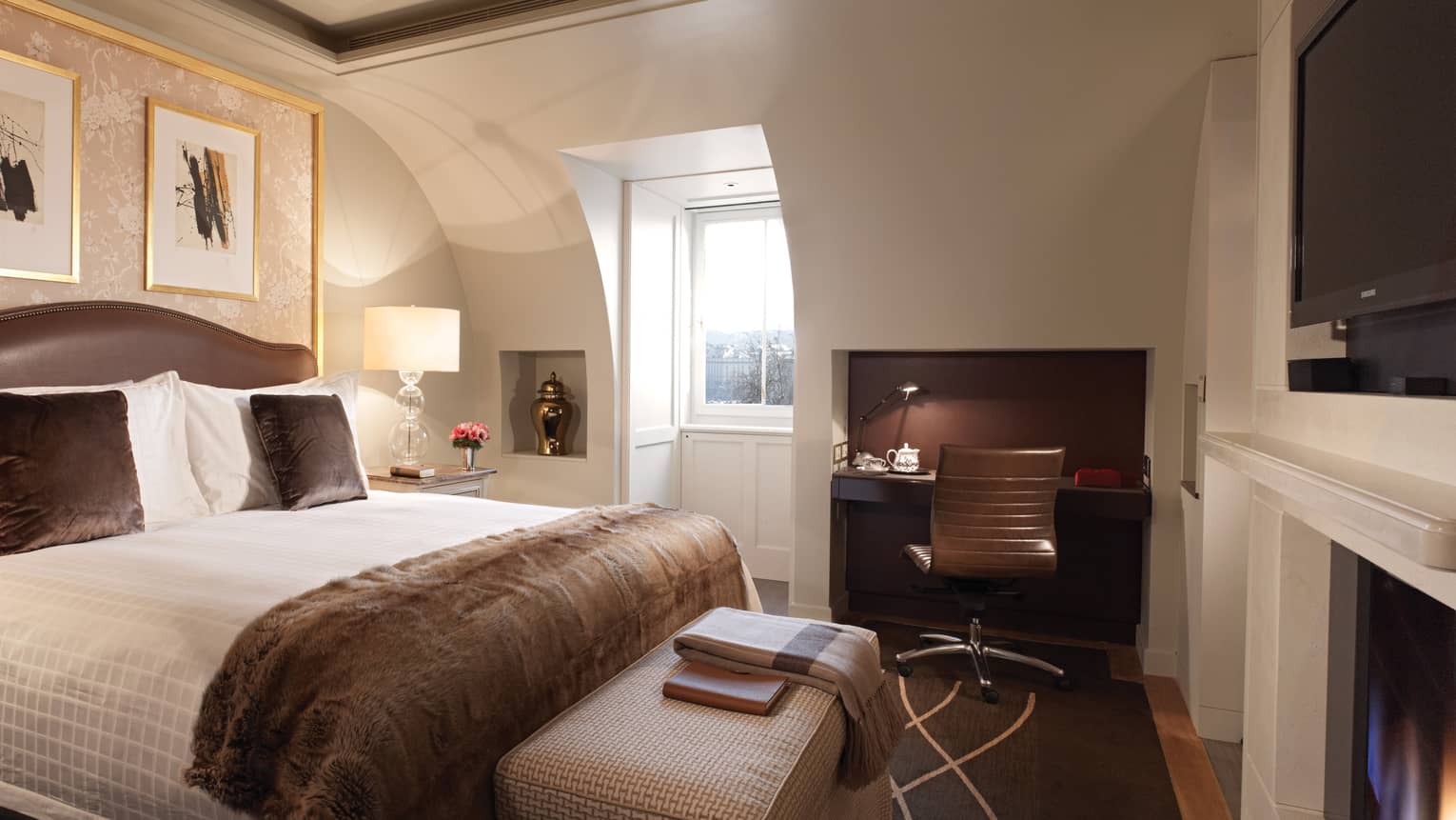 Loft studio with sloped wall and ceiling, recessed window beside bed with dark brown accent pillows, throw blanket, area rug