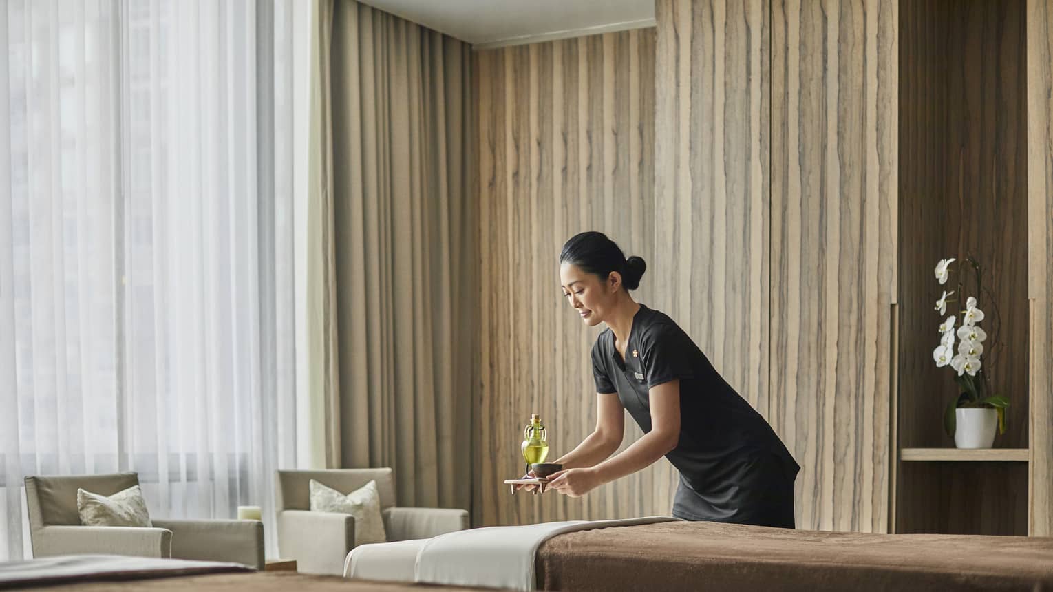 A female masseuse brings a drink to sit behind one of two massage beds. 
