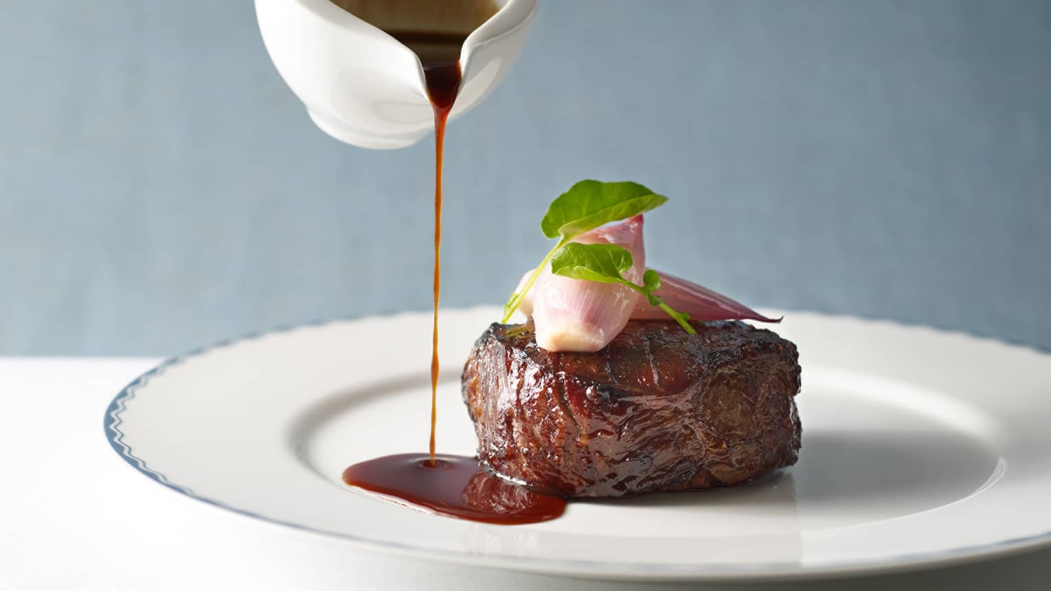 Steak with a dark red sauce being poured onto the plate.