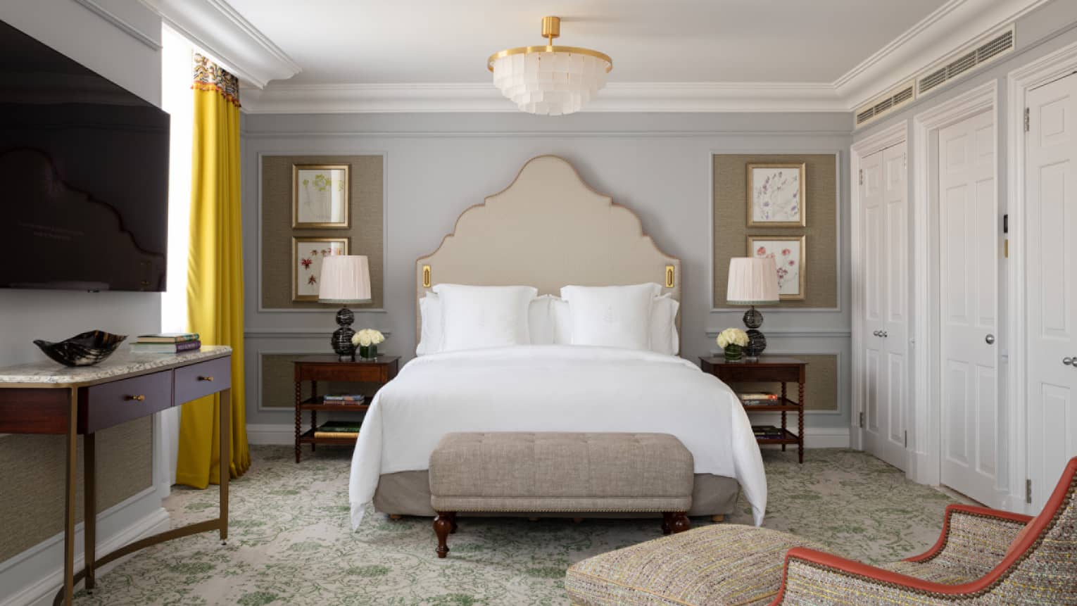 Guest room with Queen bed with white linens, cream-coloured headboad and bench at food of bed, tan chaise, flat screen TV, window with yellow drapes