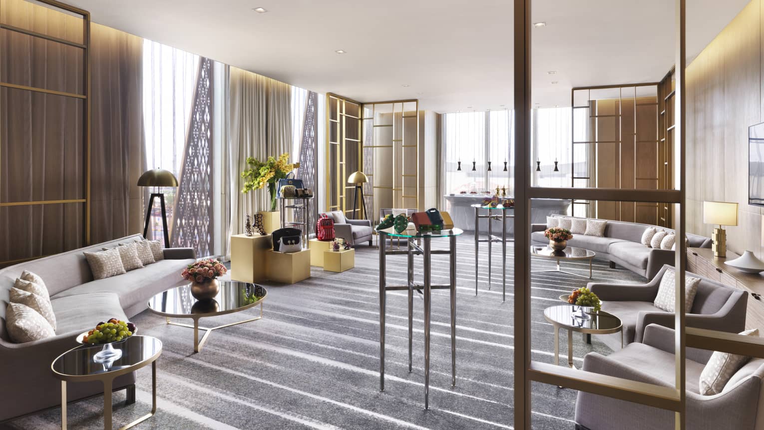 Al Qibla Lounge with mid-century style grey sofas, round glass-and-bronze tables and various bronze lamps and flowers on each table